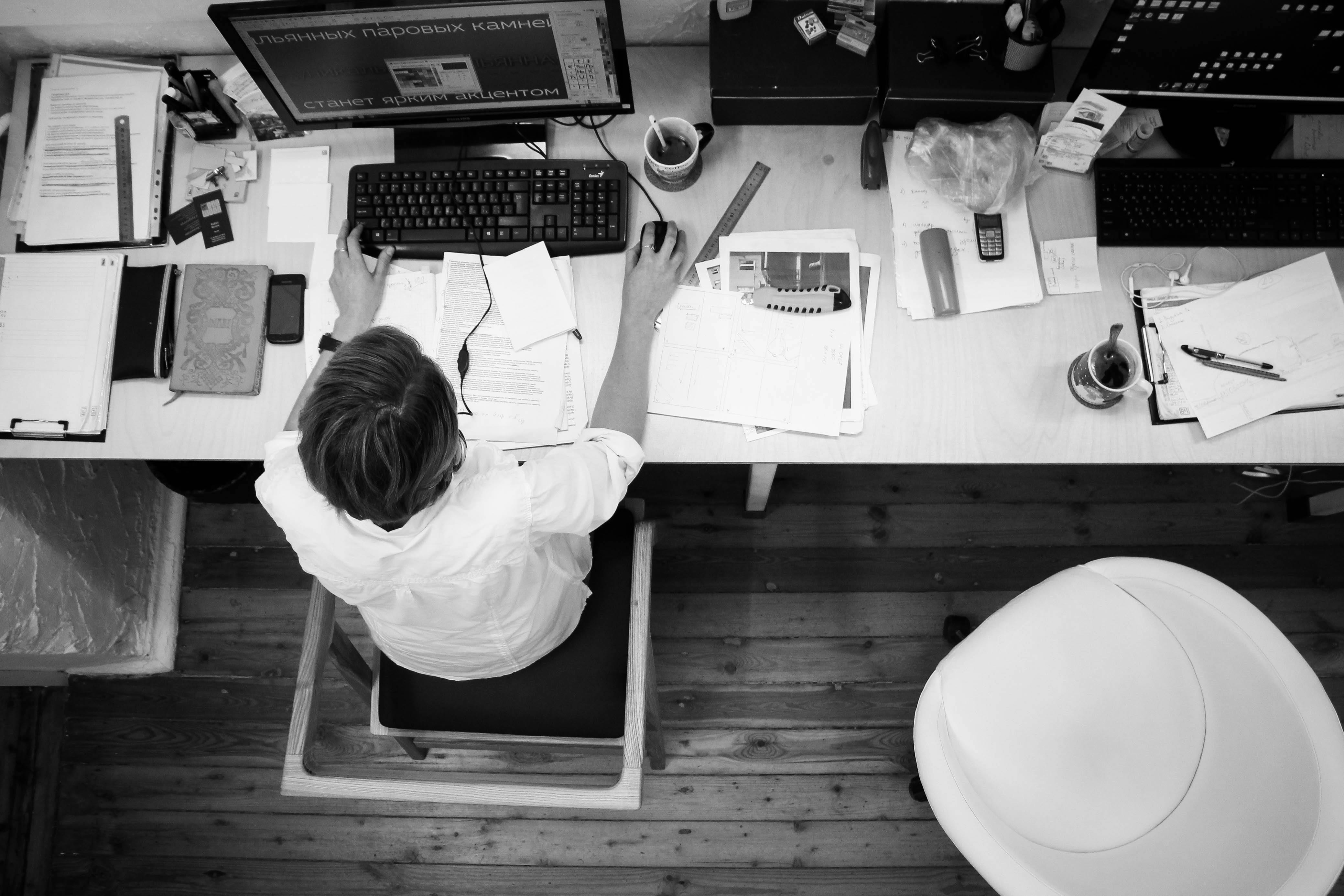 Overhead view of a person working at a desk with multiple screens and papers, representing in-depth research and analysis